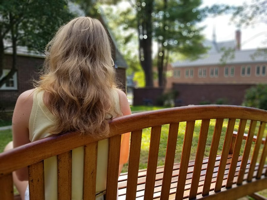 A quarantined student sits on a bench in the Muskie Garden after receiving approval to go outside. 