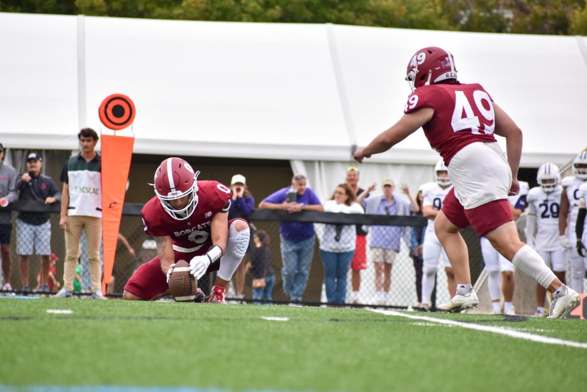 Marcos Ruiz '27 preparing to kick the winning field goal in overtime while Sergio Beltran '26 secures the ball during the Bates versus Amherst football game.